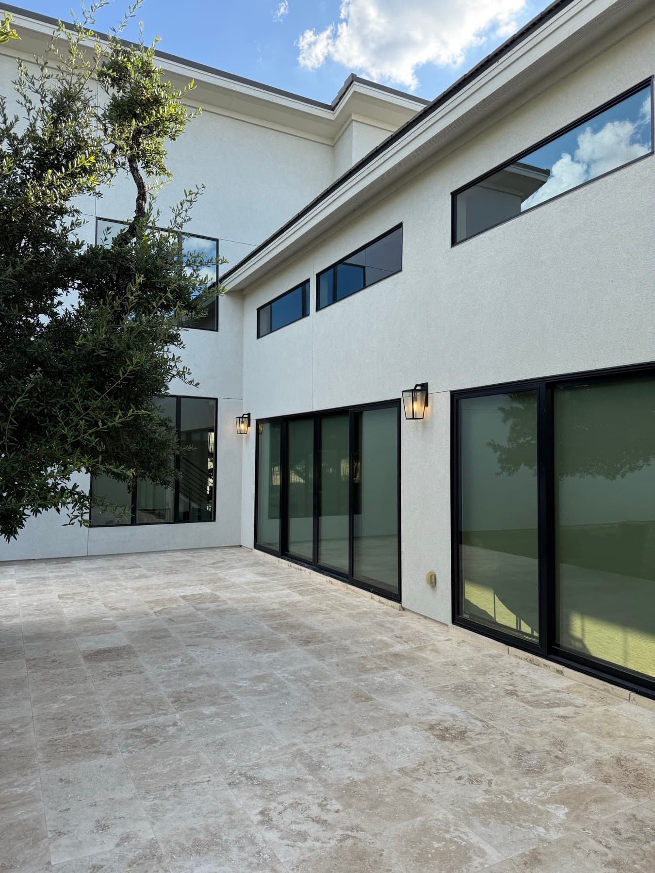 A travertine tile patio running up to the sliding glass doors of a two-story home