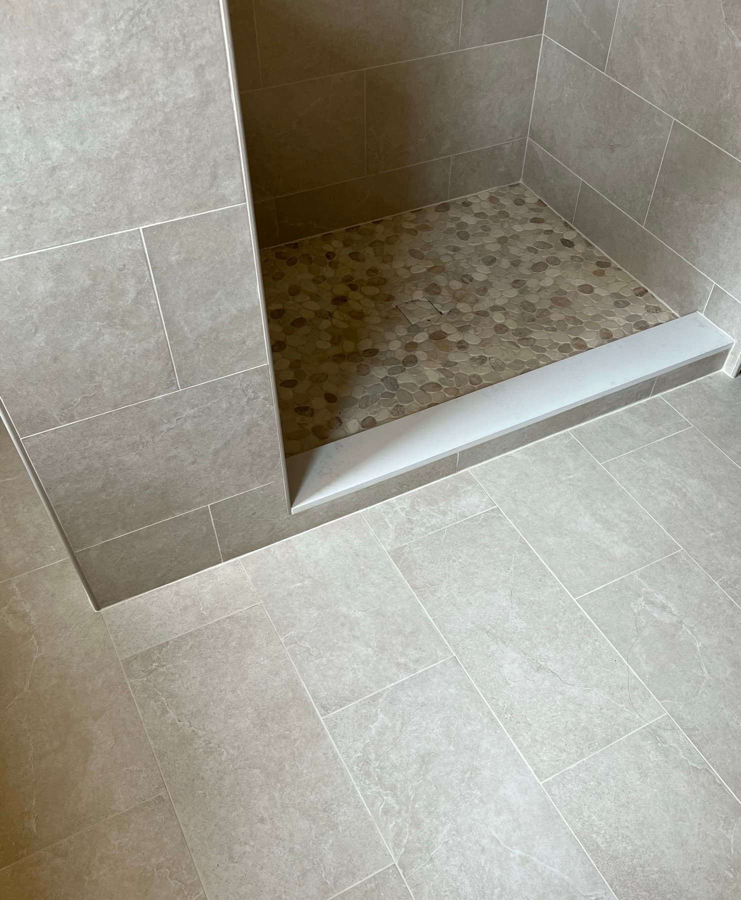 A pebble-stone shower pan sloped to its drain, with a stone curb, in an Altadena bathroom