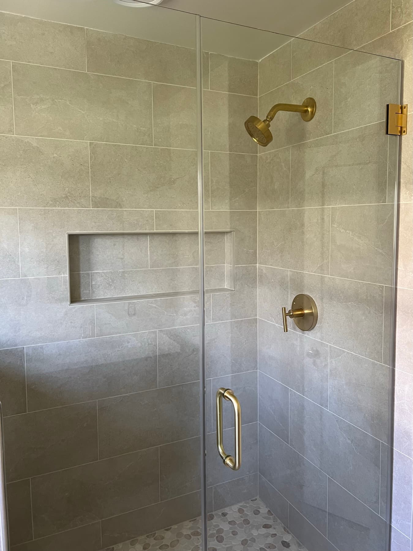 Gold shower fixtures and the recessed niche trimmed in sand-toned Schluter QUADEC, seen through the gold-hardware glass.