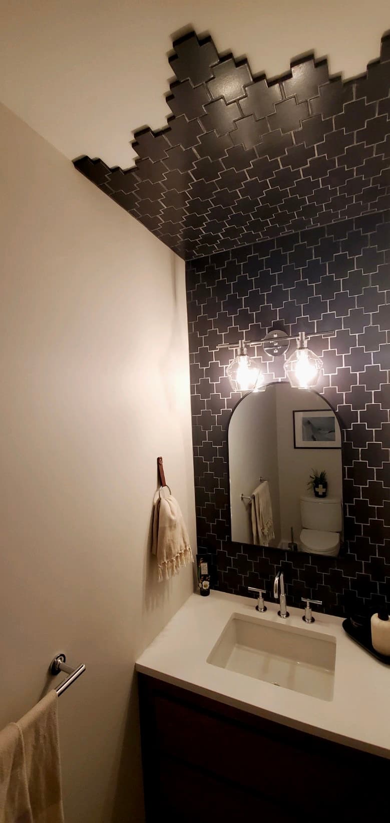 Dark cross-pattern zellige tile climbing a powder room wall onto the ceiling in a stepped, hand-cut edge
