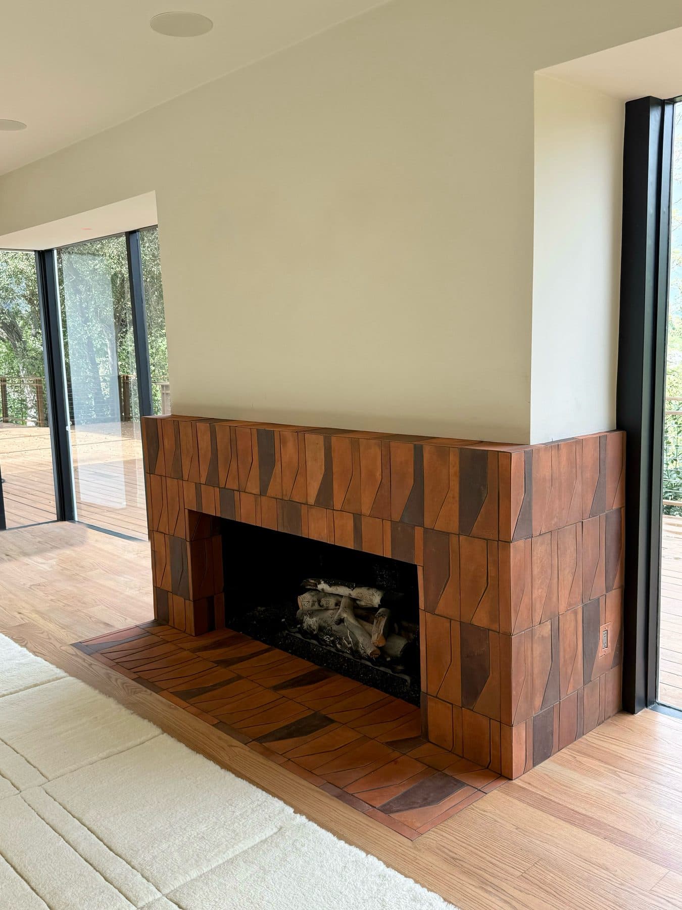 The fireplace in the room, between floor-to-ceiling windows onto the deck, the terracotta hearth set into the wood floor.