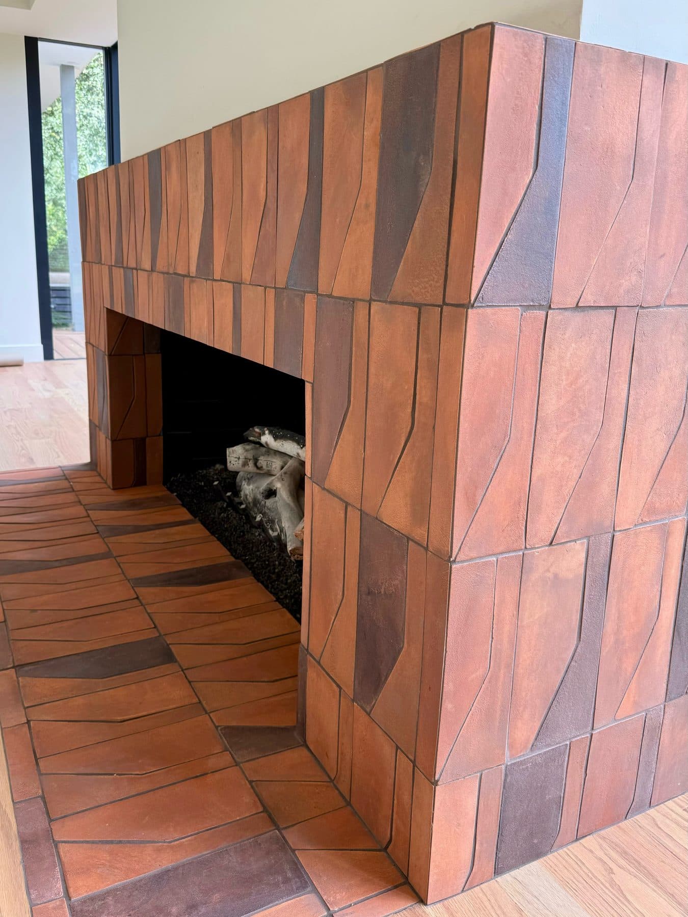 The outside corner of the surround, every edge mitered so the tile turns the corner with no trim, the hearth pattern running into the wall.