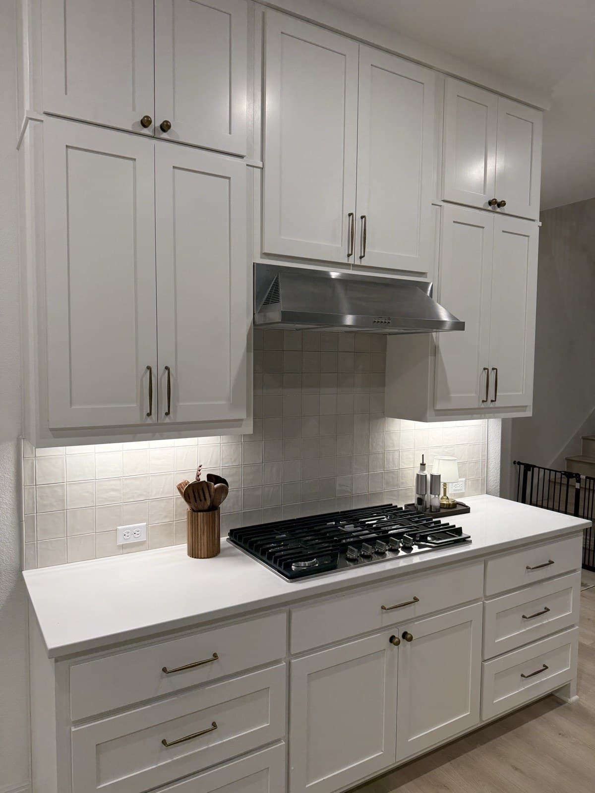 Cream 4x4 zellige stacked in a grid behind the gas cooktop, replacing the dated blue tile in a white shaker kitchen.