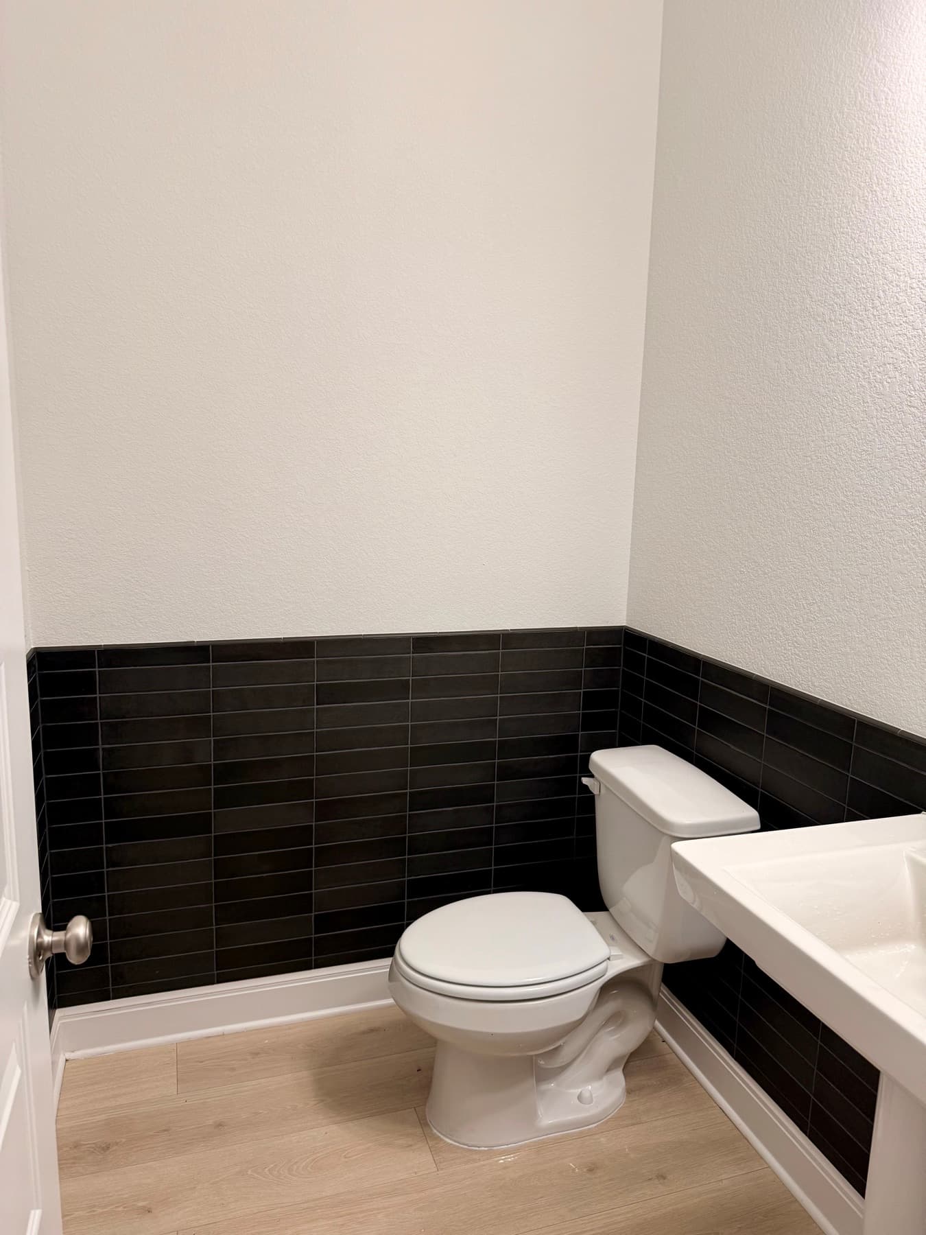Black ceramic wainscot in the half bath, stacked in thin horizontal courses and wrapped around the corner at chair-rail height.