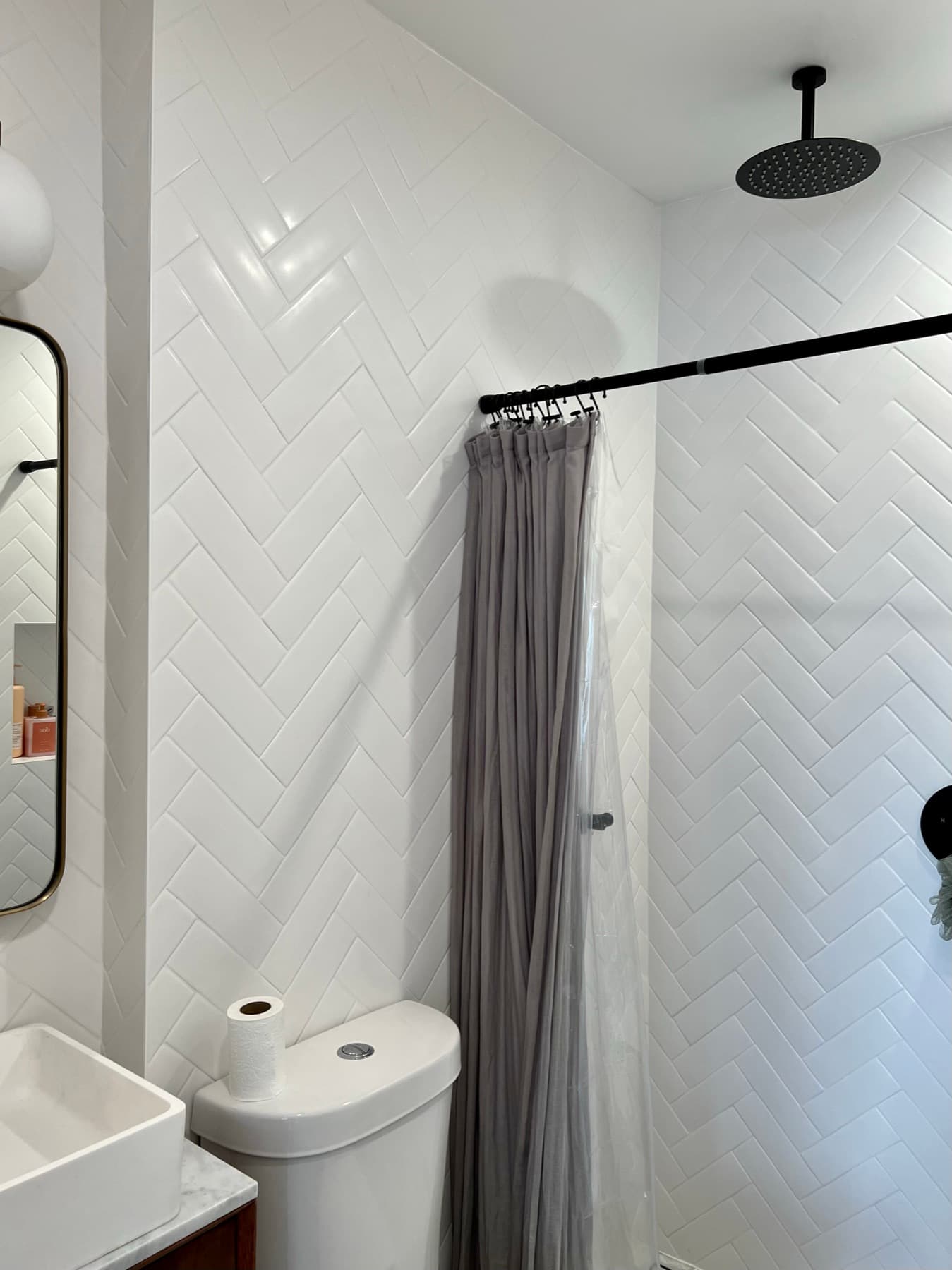 Shower corner · the herringbone pattern carries across wall planes, matte-black rain head overhead