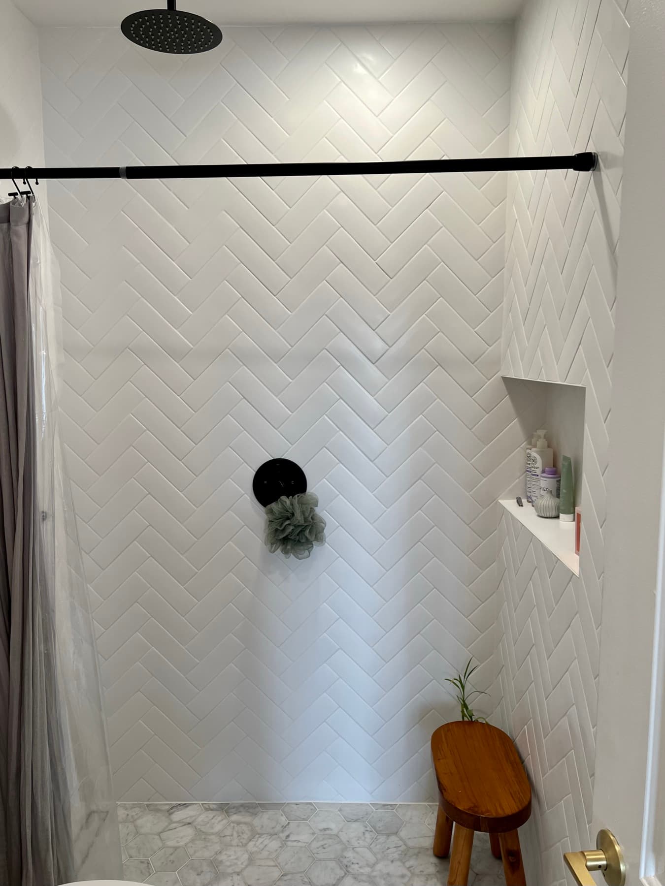 The finished shower: herringbone walls, tiled niche, marble hexagon floor, and curbless entry