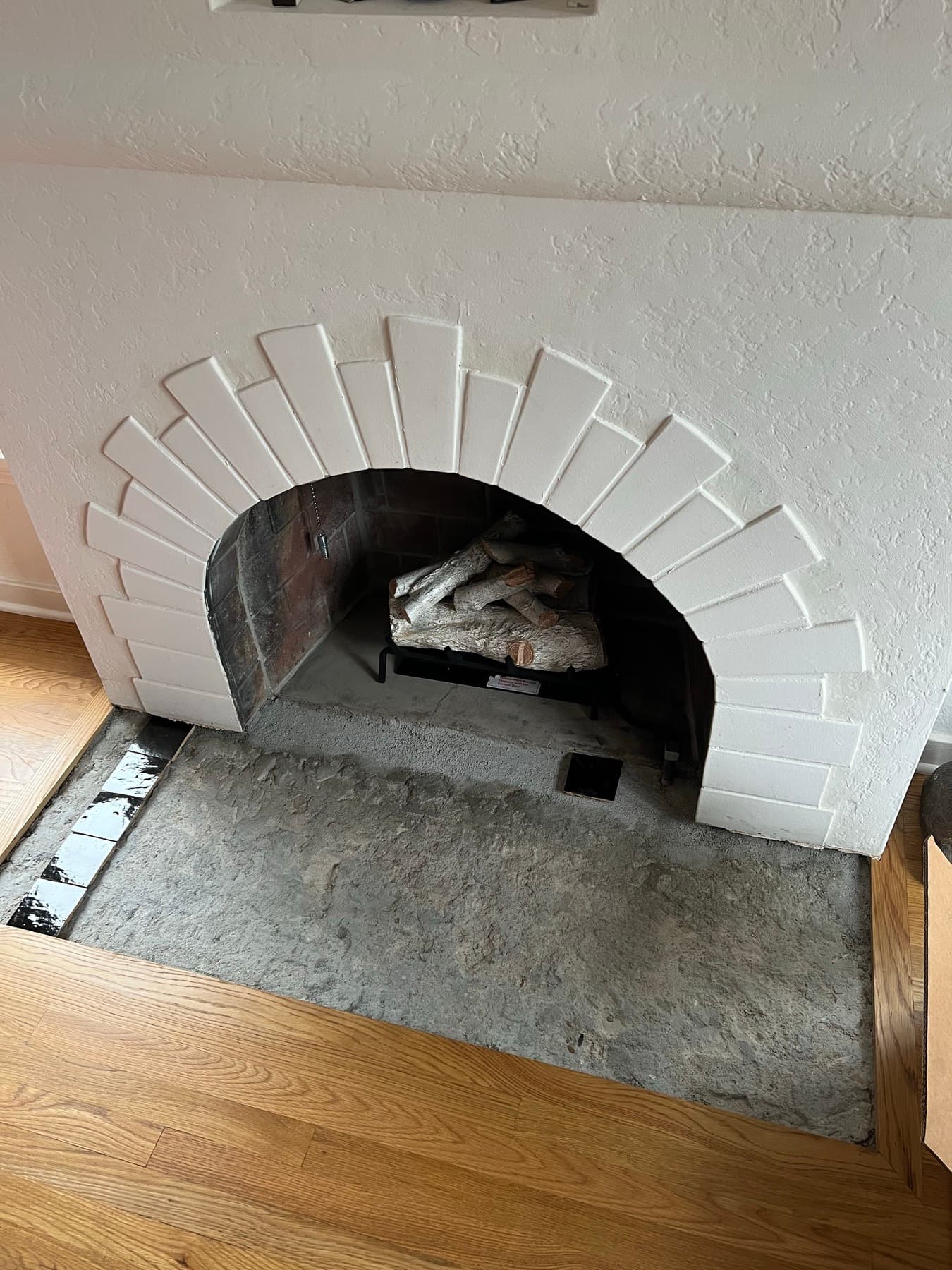 The fireplace mid-install, the hearth stripped back to the slab with the first row of black zellige set along the edge.