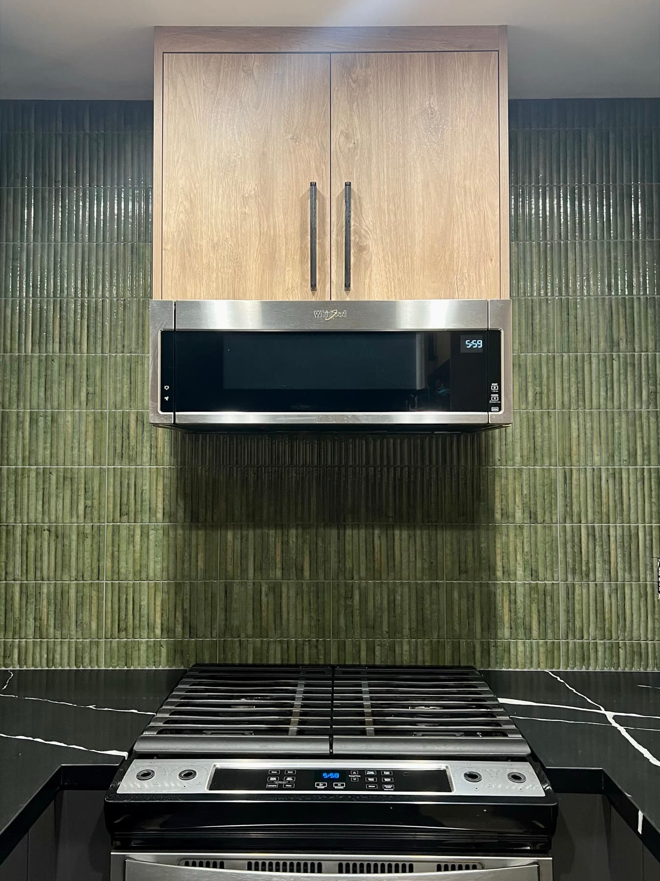 Olive green kit-kat ceramic run full height behind a range, under oak cabinetry and against black stone counters, in a Los Angeles kitchen