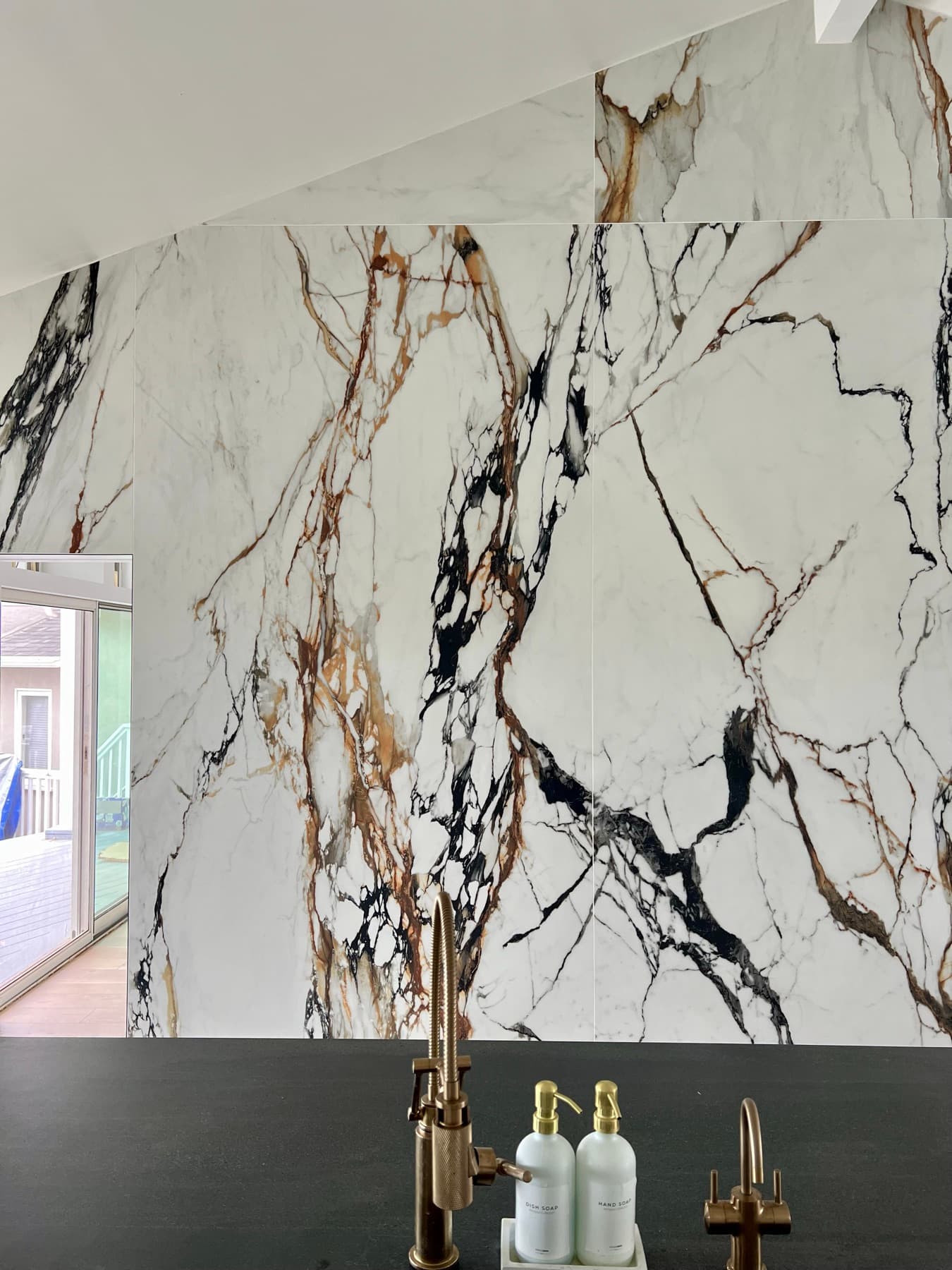 The primary slab wall seen across the dark island, with brass fixtures below and the veining running unbroken to the ceiling.