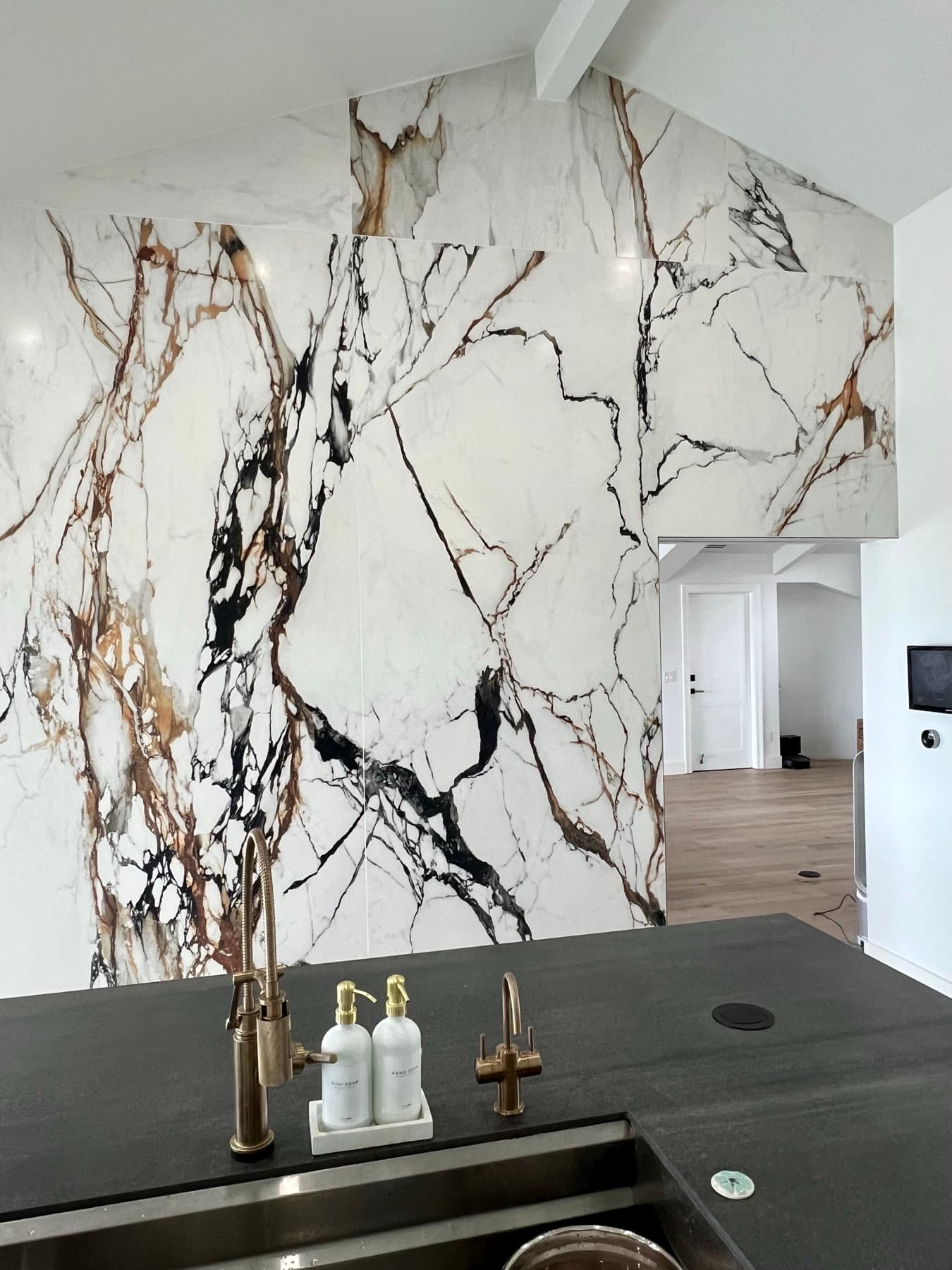 A full-height marble-look porcelain slab wall meeting a dark stone island and brass fixtures in a modern Los Angeles kitchen