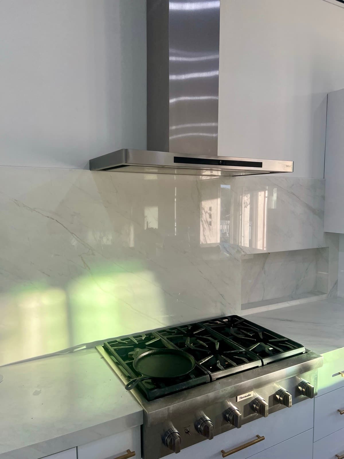 The cooktop backsplash, a single porcelain slab matched to the existing countertop, behind a stainless hood.