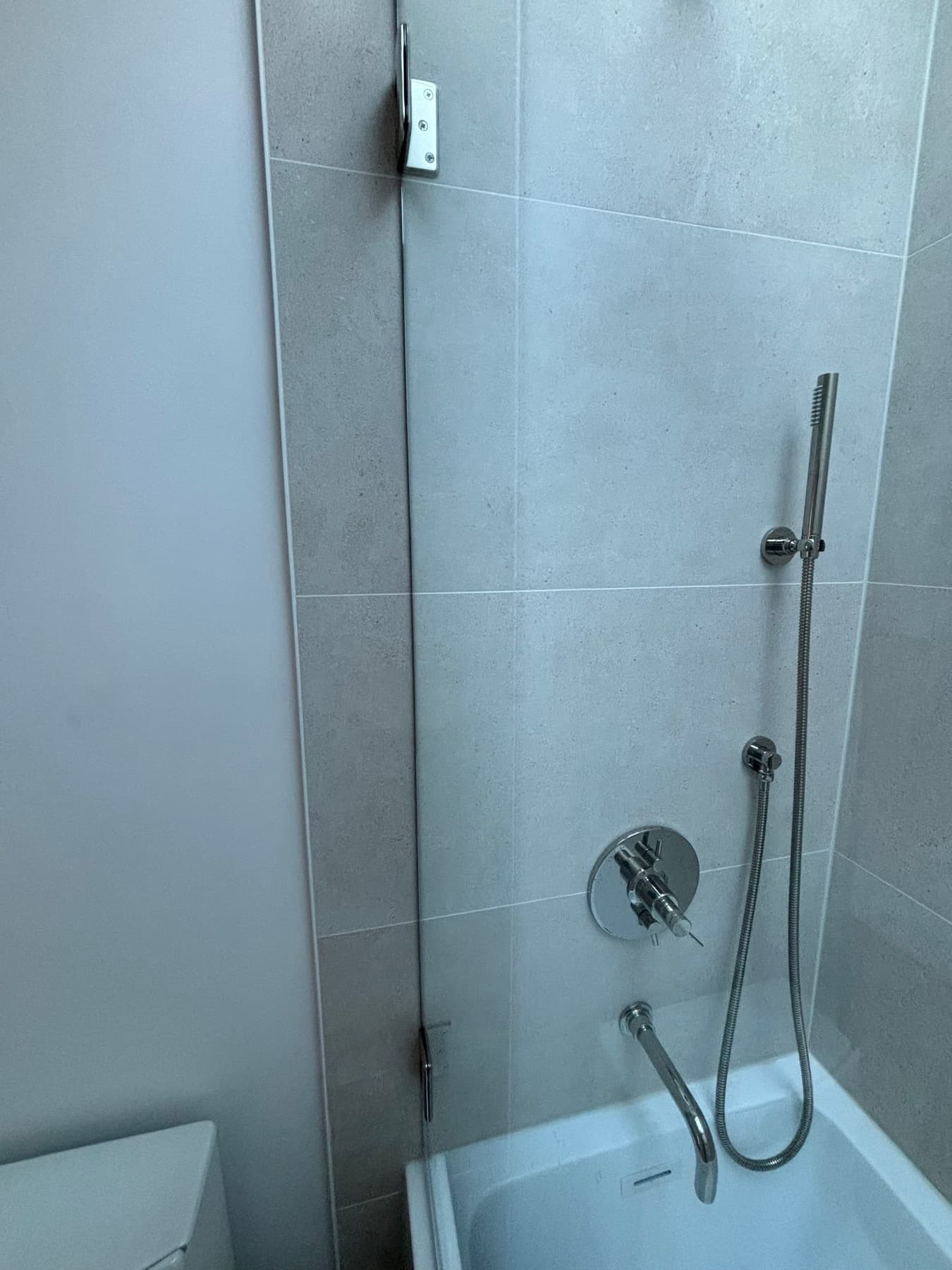Kohler chrome shower set · handheld, valve, and tub spout behind the fixed glass panel