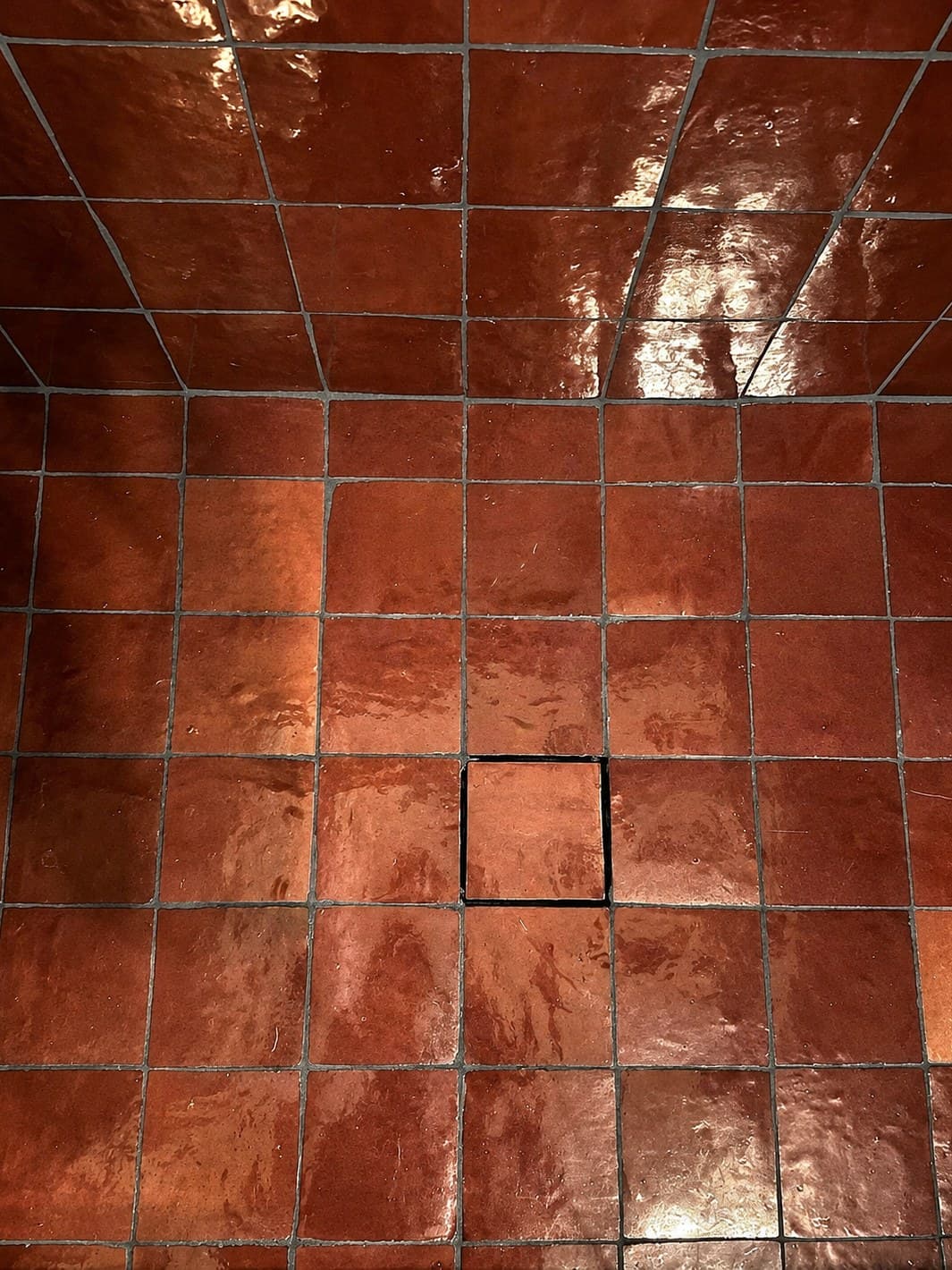 The rouge zellige shower floor, with a tile set into the Schluter tileable drain grate at the center.
