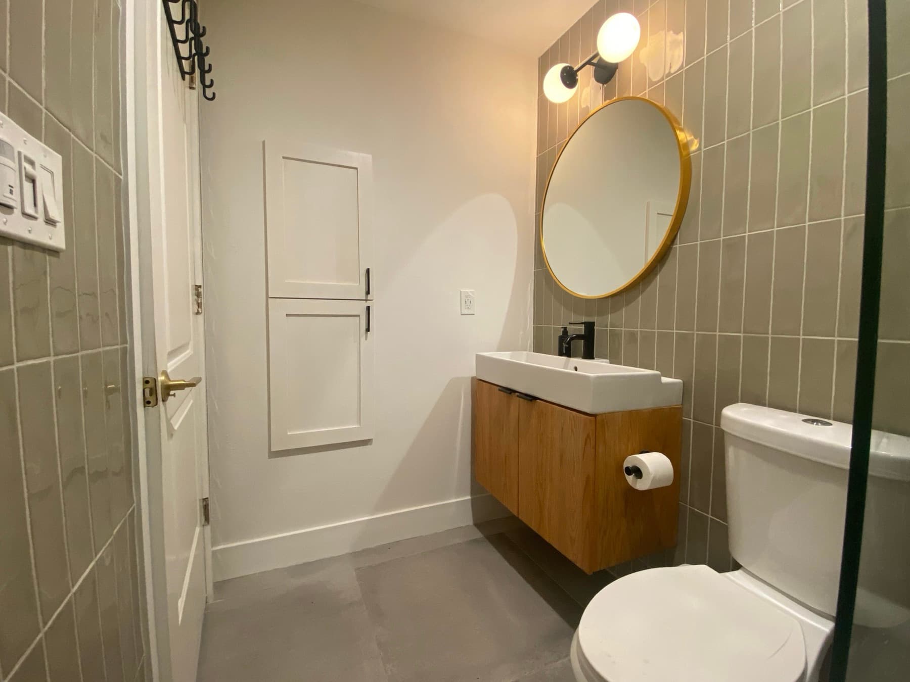 A wider view of the vanity wall, with the 24×24 grey porcelain floor running to the door.